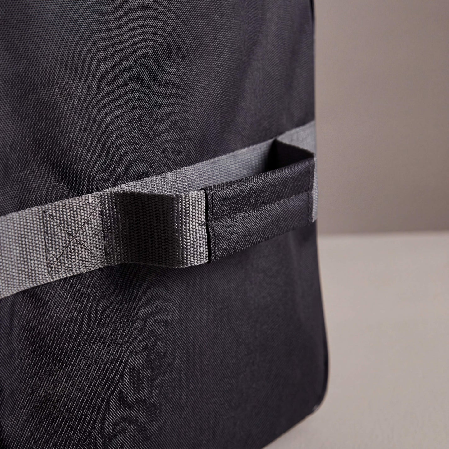 Close-up of a black backpack with a gray strap on a neutral background