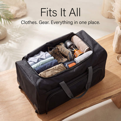 Black travel duffel bag with clothes and gear on a wooden surface.