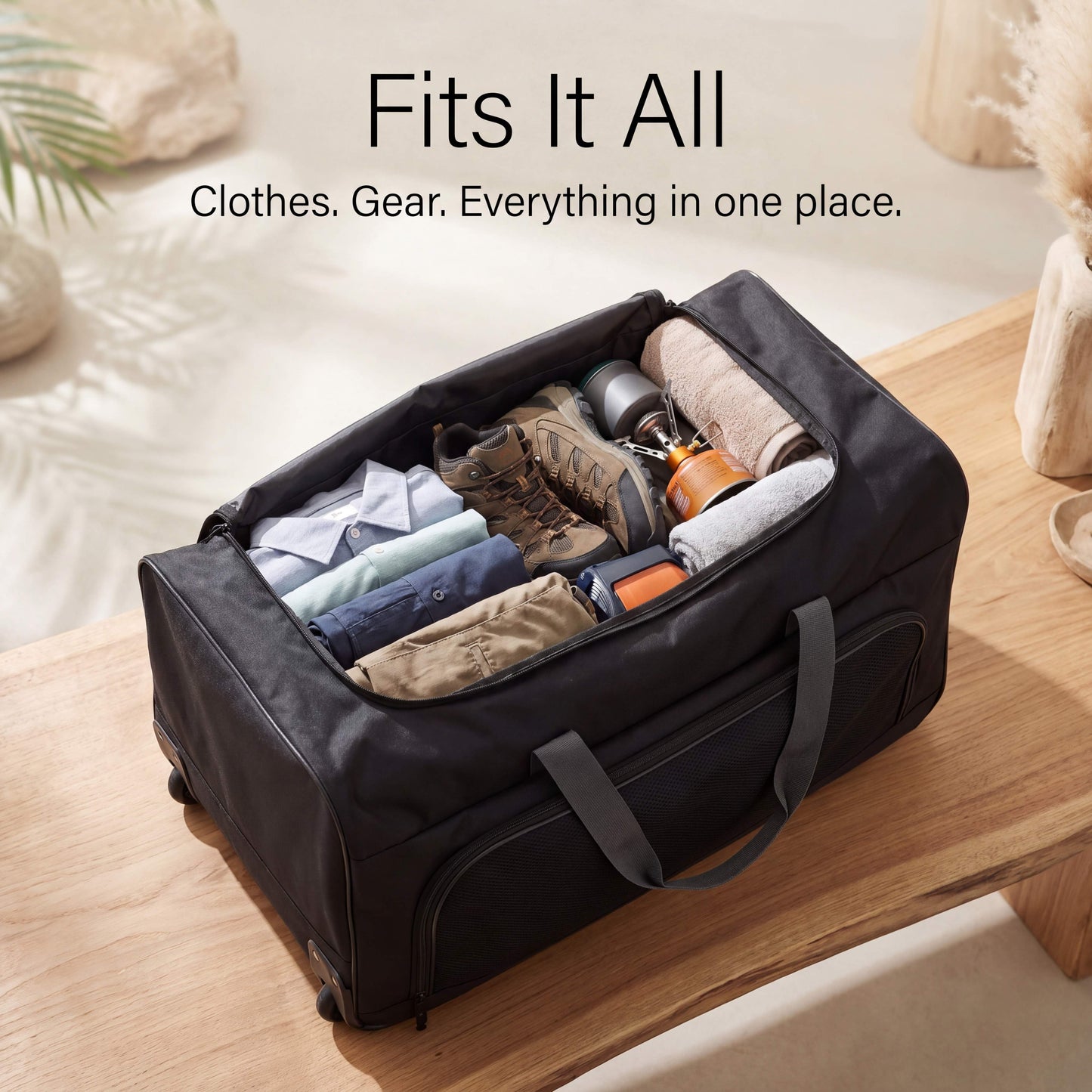 Black travel duffel bag with clothes and gear on a wooden surface.