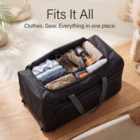 Black travel duffel bag with clothes and gear on a wooden surface.