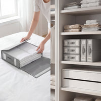 Person organizing folded clothes into a gray storage bag, with shelves in the background.