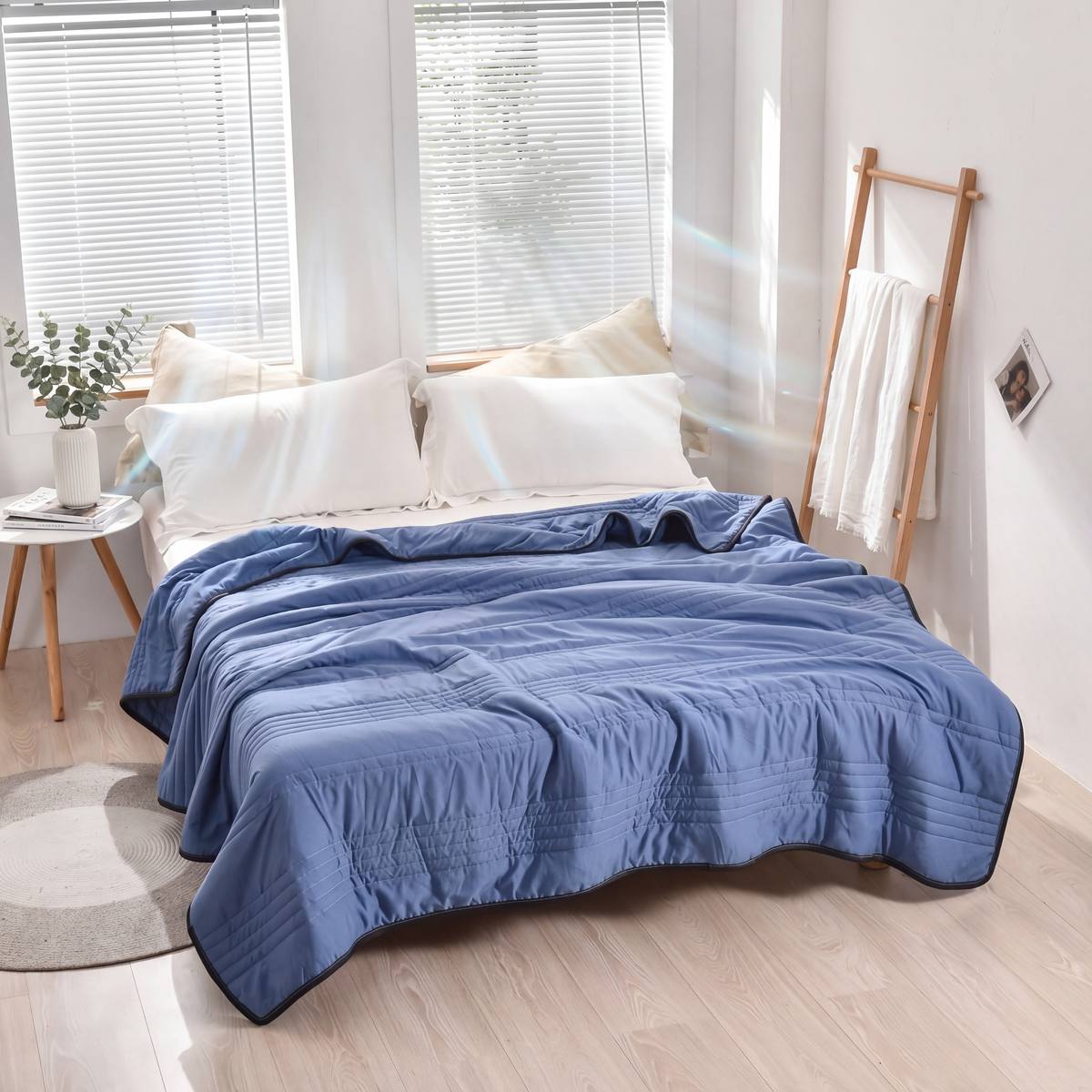 Blue quilt on a bed in a bright bedroom with white walls and wooden floor.