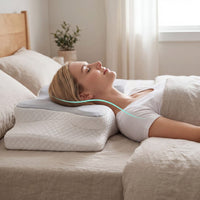 Woman lying on a bed using an ergonomic pillow in a bedroom setting.