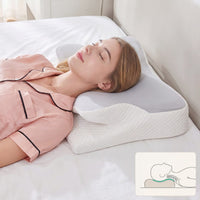 Woman lying on a white bed with a white pillow, wearing pink pajamas.