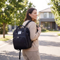 Woman with a black backpack walking outdoors on a sunny day.