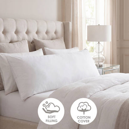 White bedding set on a bed with a tufted headboard and lamp in a bedroom setting.